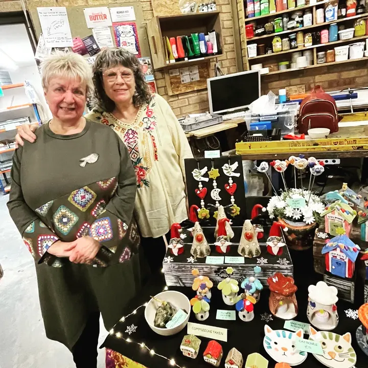 Two makers beside a table of ceramic gnomes, birds and cat bowls